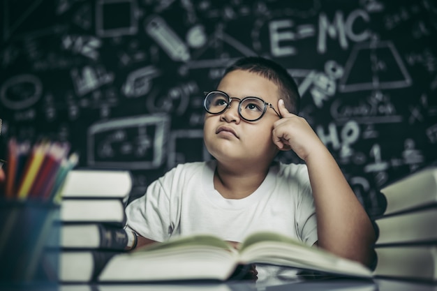 眼鏡をかけた男の子が本を書いて教室で考える