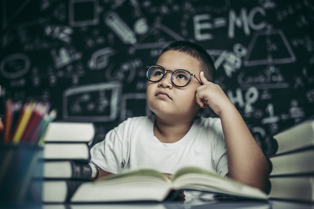 眼鏡​を​かけた​男の子​が​本​を​書いて​教室​で​考える