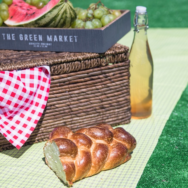 Free photo braided baked bread; fresh fruits and picnic basket on cloth