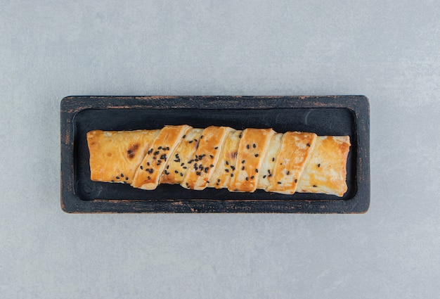 Braided bun with sesame seeds on black plate. 