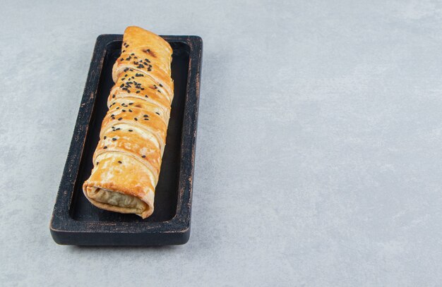 Braided bun with sesame seeds on black plate. 