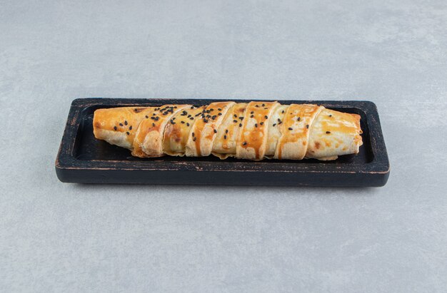 Braided bun with sesame seeds on black plate. 