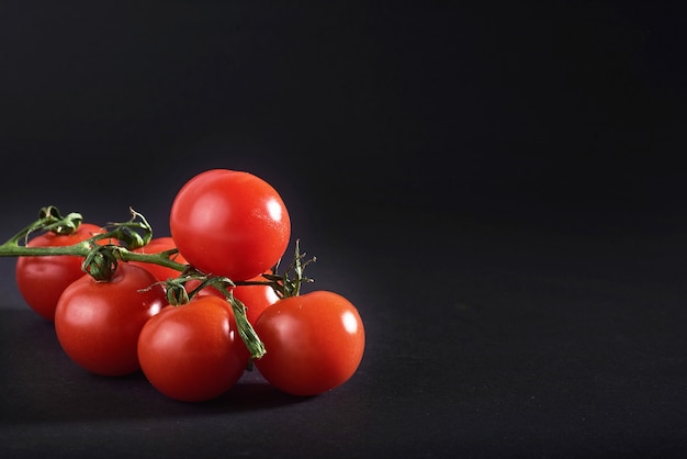 Branch of red organic tomatoes on a black