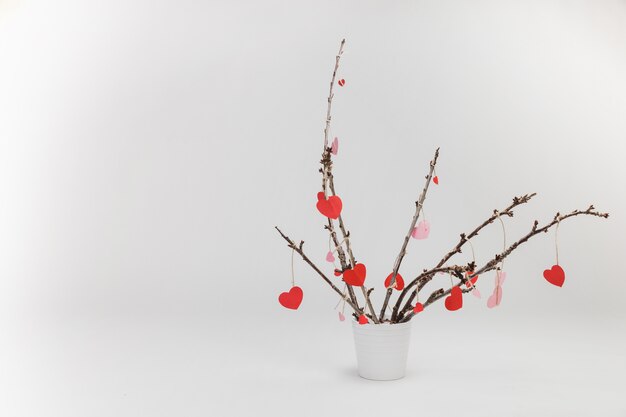 Branches of a plant in a white flowerpot with hanging hearts