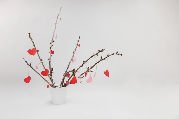 Branches of a plant in a white flowerpot with hanging hearts