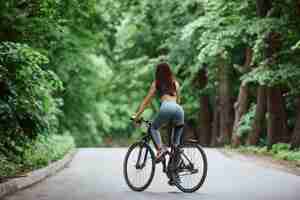 Free photo brand new bike. female cyclist on asphalt road in the forest at daytime