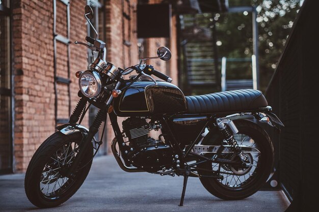 Brand new, shiny black retro chopper is parked next to brick building.