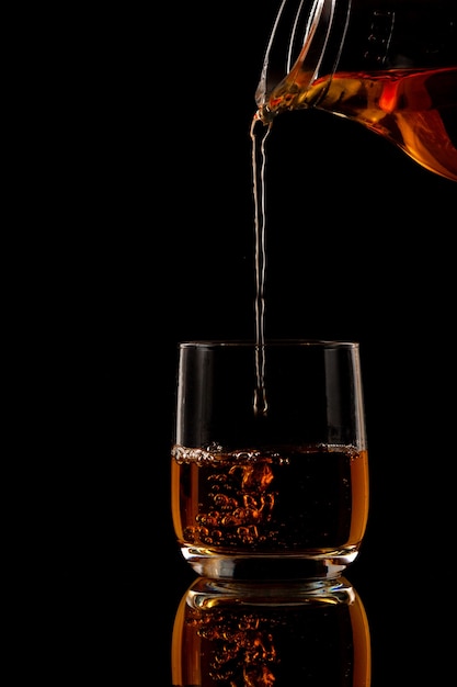 Brandy is poured into a glass on a black background Premium Photo