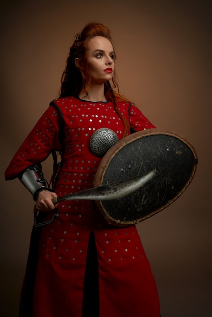 Brave woman in medieval tunic posing with weapon.