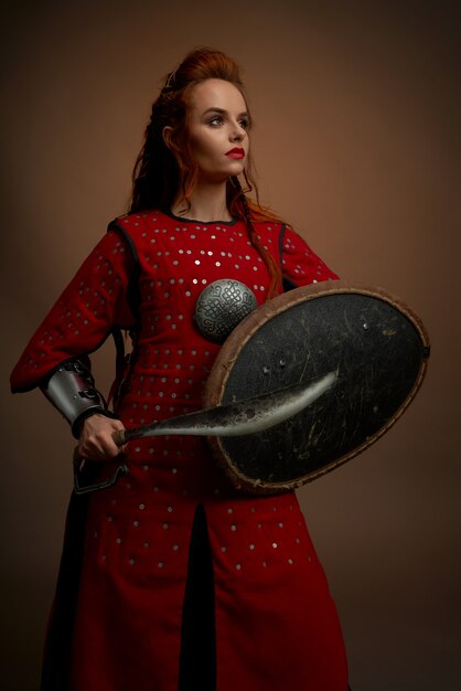 Brave woman in medieval tunic posing with weapon.