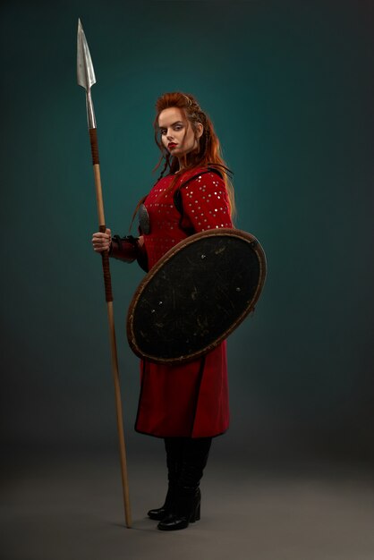 Brave woman warrior with weapon posing in studio.