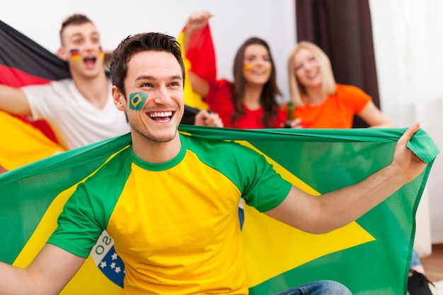 Бразильский мужчина с друзьями из разных стран наслаждается футболом по телевизору