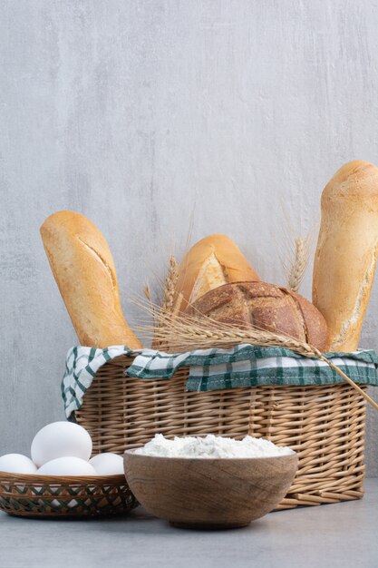 Bread basket, egg and flour on stone surface