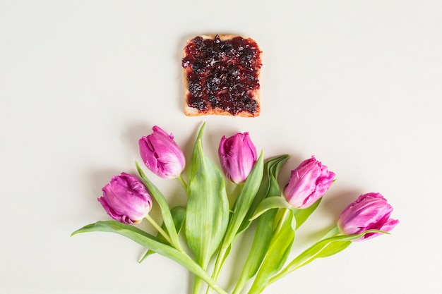 Bread and berry jam over the purple tulips on white background