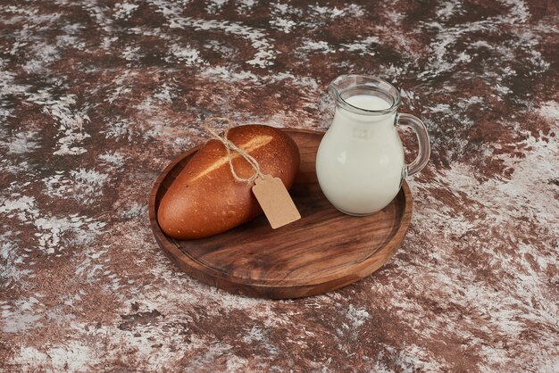 Bread bun on marble on wooden board with a jar of milk.