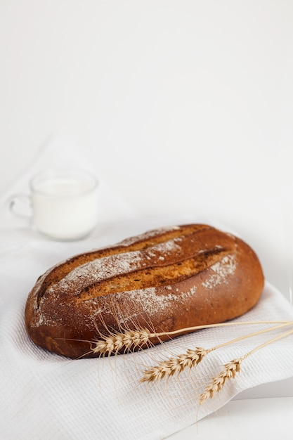 The bread is lying on a white napkin. next to him are wheat ears  a mug of milk. selective focus.