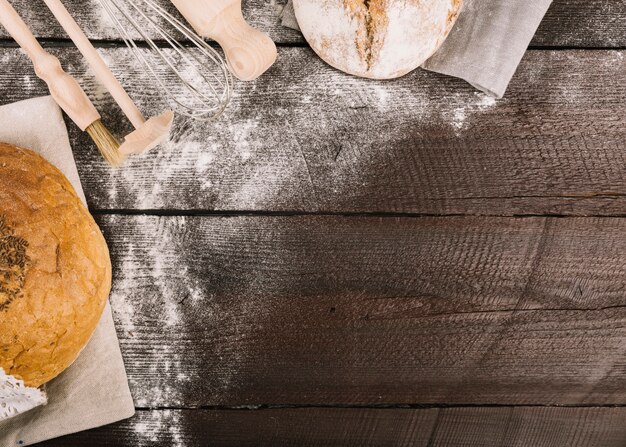 Bread and kitchen tools dusted with flour on wooden plank