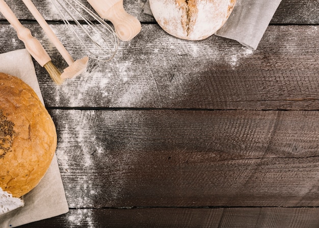 Bread and kitchen tools dusted with flour on wooden plank