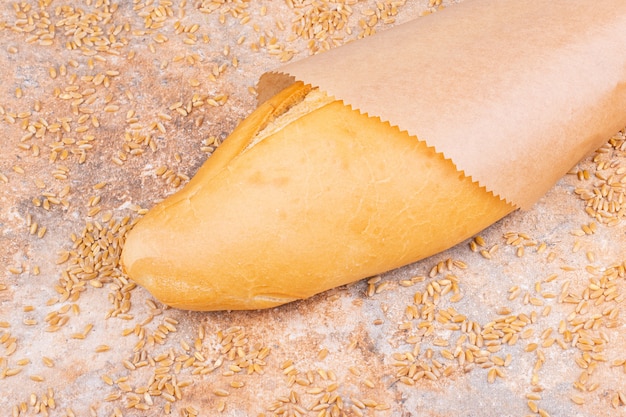 Foto gratuita pane in un sacchetto di carta accanto al chicco di grano cosparso, sul tavolo di marmo.