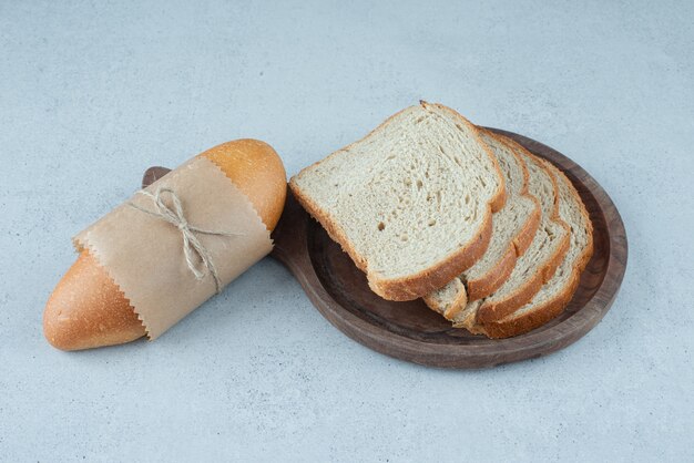 Bread roll and bread slices on wooden plate