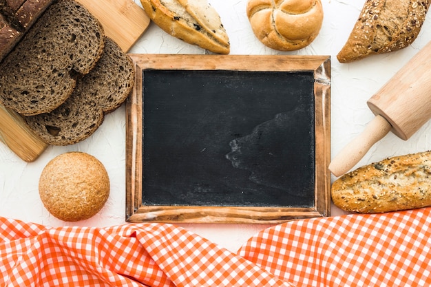 Bread and rolling pin near blackboard and cloth