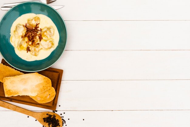 Bread slice and creamy ravioli pasta with white sauce on wooden surface