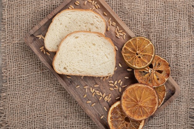 Бесплатное фото Ломтики хлеба и сушеный апельсин на деревянной тарелке. фото высокого качества