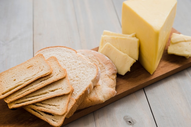 Bread slices and cheese wedges on chopping board over the table