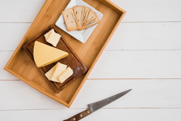 Bread slices and cheese wedges on wooden tray with knife