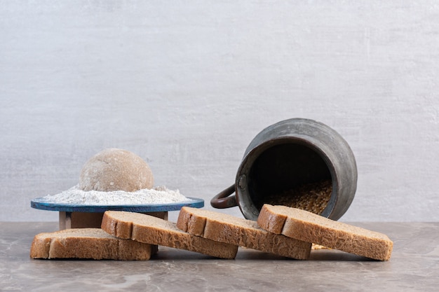 Free photo bread slices, flour platter and jug of wheat on marble.