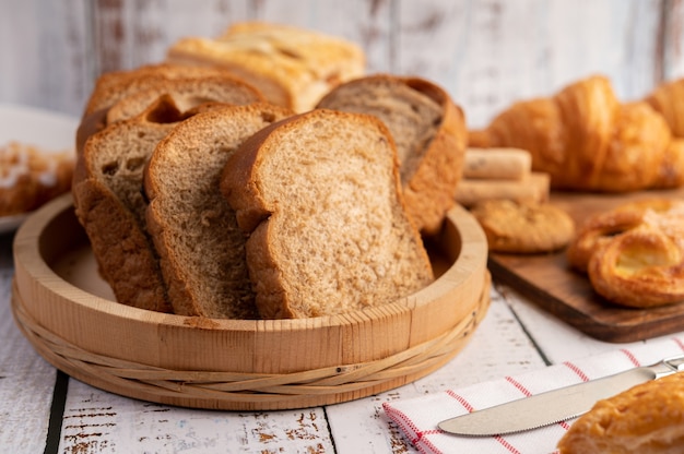 Ломтики хлеба размещены в деревянной тарелке на белом деревянном столе.