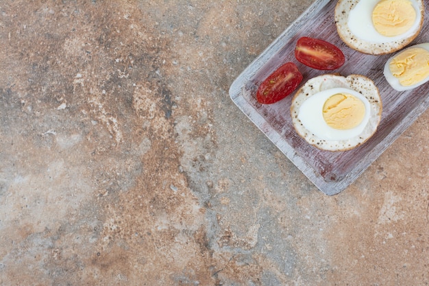 Free photo bread slices with boiled eggs and tomato slices on wooden board