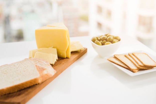 Bread slices with cheese and olives on white table
