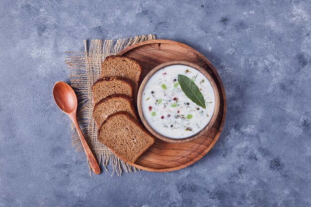 Bread slices with a cup of yogurt soup and oregano leaf.