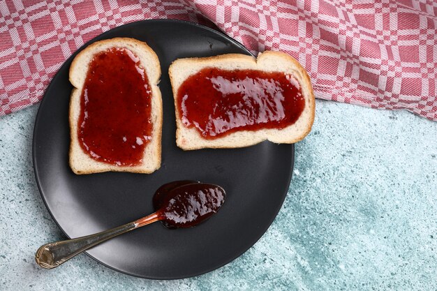 Bread slices with strawberry jam in grey plate with a spoon of jam. Top view.