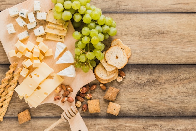 Bread sticks, cheese blocks, grapes, bread and cookies on wooden desk