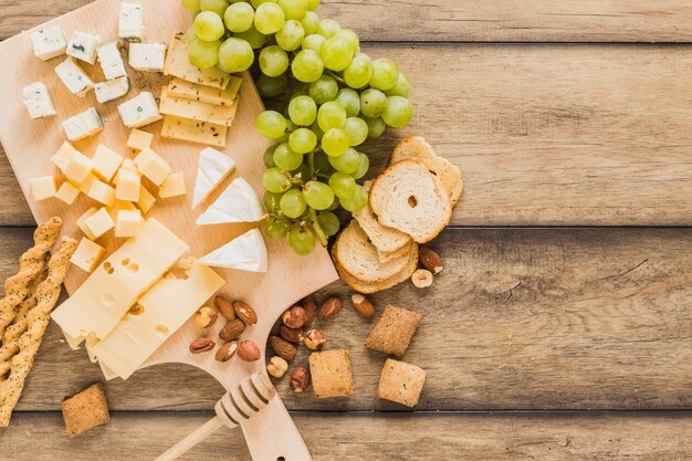 Bread sticks, cheese blocks, grapes, bread and cookies on wooden desk