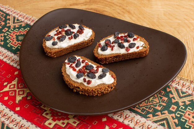 bread toasts with dried fruits inside dark plate on wooden desk