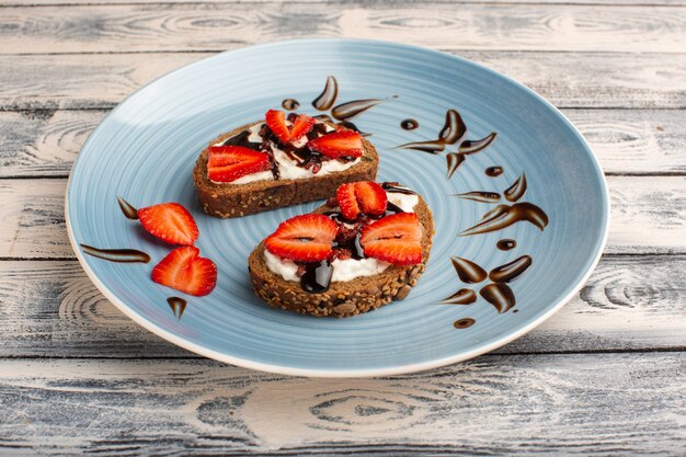 bread toasts with sour cream and sliced strawberries on wood