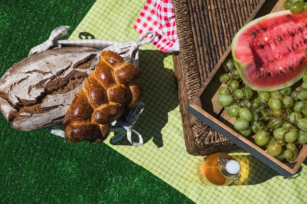 Bread; watermelon; grapes and olive oil bottle on blanket over turf at picnic