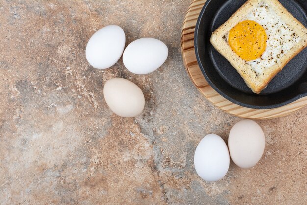 Bread with fried eggs on black plate with raw eggs