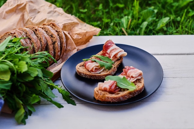 Bread with ham and herbs on a black plate on a wooden table.
