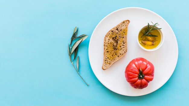 파란색 배경 위에 접시에 빨간 토마토와 로즈마리와 마늘 정향 기름 빵