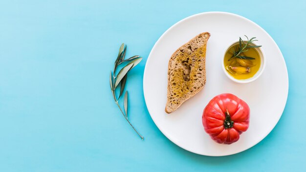 Bread with rosemary and garlic clove oil with red tomato on plate over the blue backdrop