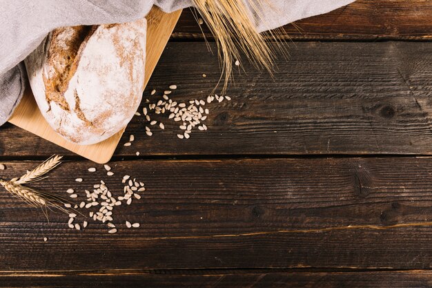 Bread with sunflower seeds and wheat crop on wooden table