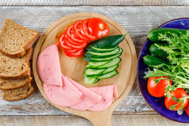 Bread with tomato, cucumber, sausage, greens flat lay on wooden and cutting board