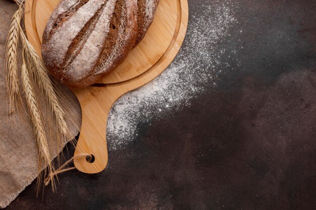 Bread on wooden board with wheat grass and flour