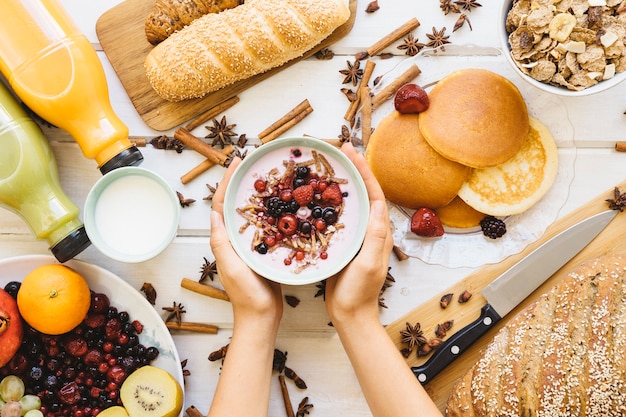 Breakfast composition with hands holding bowl of yogurt