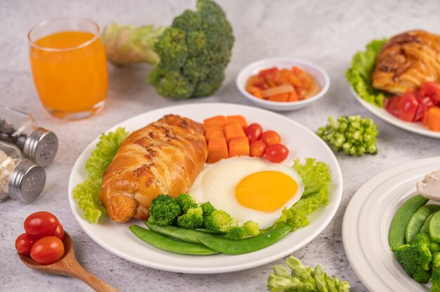 朝食は、パン、目玉焼き、ブロッコリー、ニンジン、トマト、レタスの白い皿の上で構成されます。