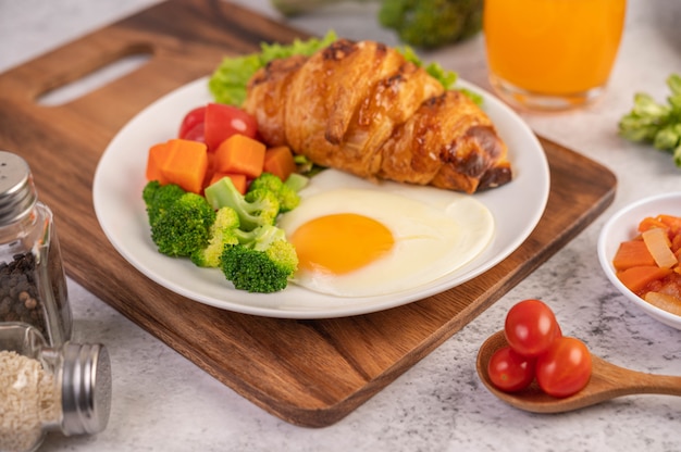 Breakfast consisting of bread, fried eggs, broccoli, carrots, tomatoes and lettuce on a white plate.